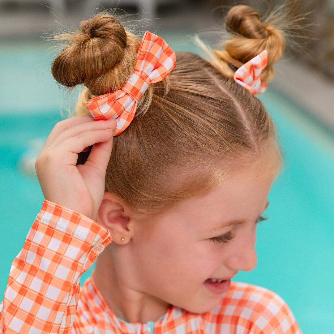 menina usando lacinho de cabelo combinando com look de praia de manga longa, na estampa Vichy Laranja da Lili Sampedro