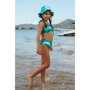 Menina de 6 anos vestindo biquíni infantil e chapéu infantil combinando na praia Tie Dye Verde da Lili Sampedro
