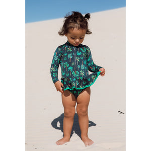 Bebe está vestindo maiozinho de praia infantil de manga longa com babadinhos e zipper na frente, na estampa coqueiros azul marinho, com protecao UV da Lili Sampedro