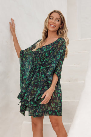 Modelo vestindo Saída de Praia Kaftan Nathy na Estampa Coqueiros com Fundo Azul Marinho, modelo tipo Kimono, fechado, curto, feito de chiffon, um tecido tipo seda, da Lili Sampedro Moda Praia Feminina